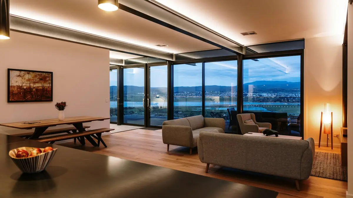 Modern living room with large windows showcasing city views and ambient lighting.