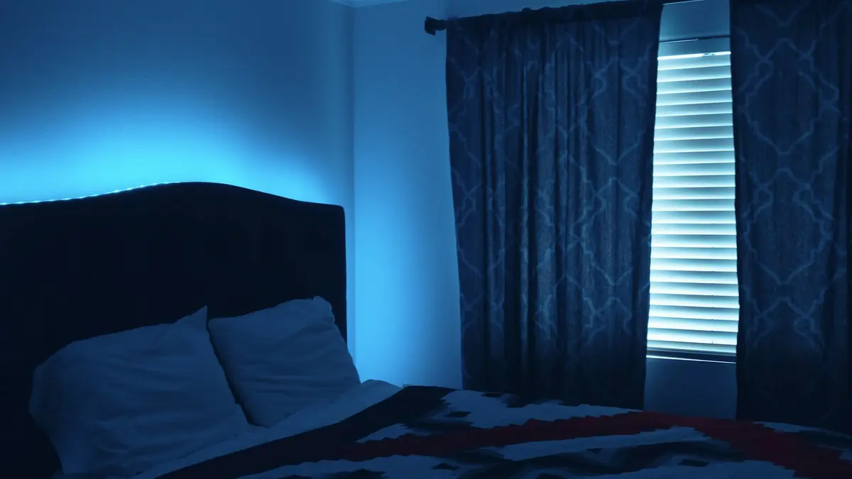 A dimly lit bedroom with blue LED lights around the bed and closed curtains.