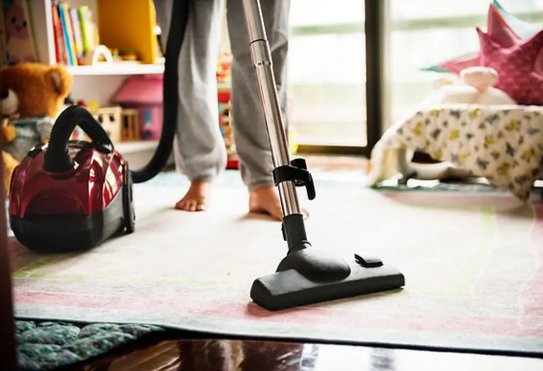Person vacuuming a carpet with bare feet and a vacuum cleaner beside them.