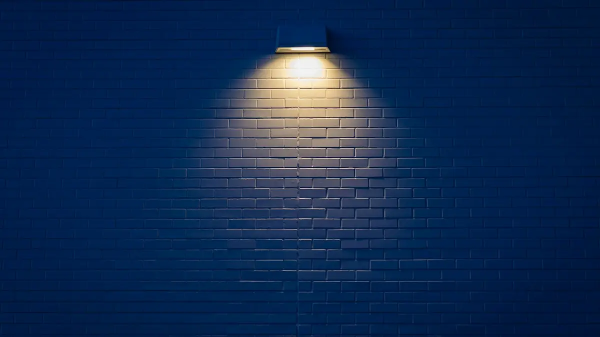 Wall-mounted light illuminating a textured blue brick wall in a dimly lit scene.