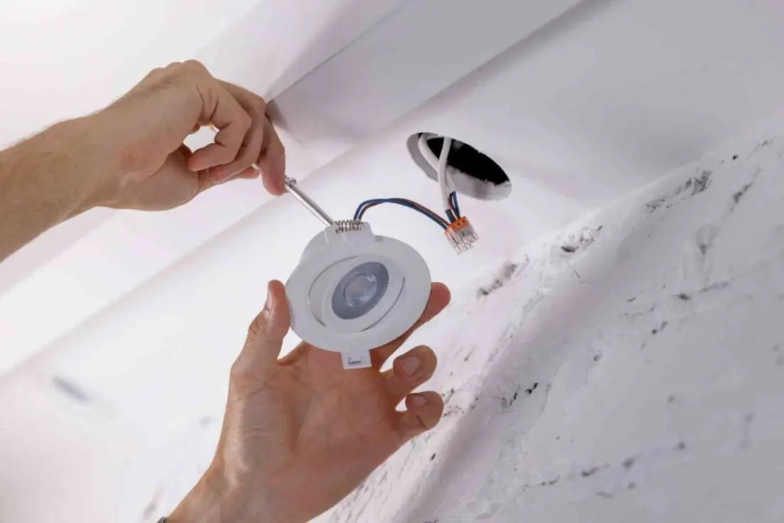 A person installing a recessed LED light fixture into a ceiling.