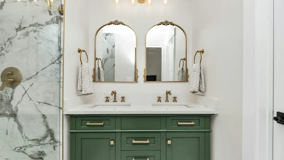 A green bathroom vanity with two sinks, featuring two gold-framed mirrors and overhead light fixtures.