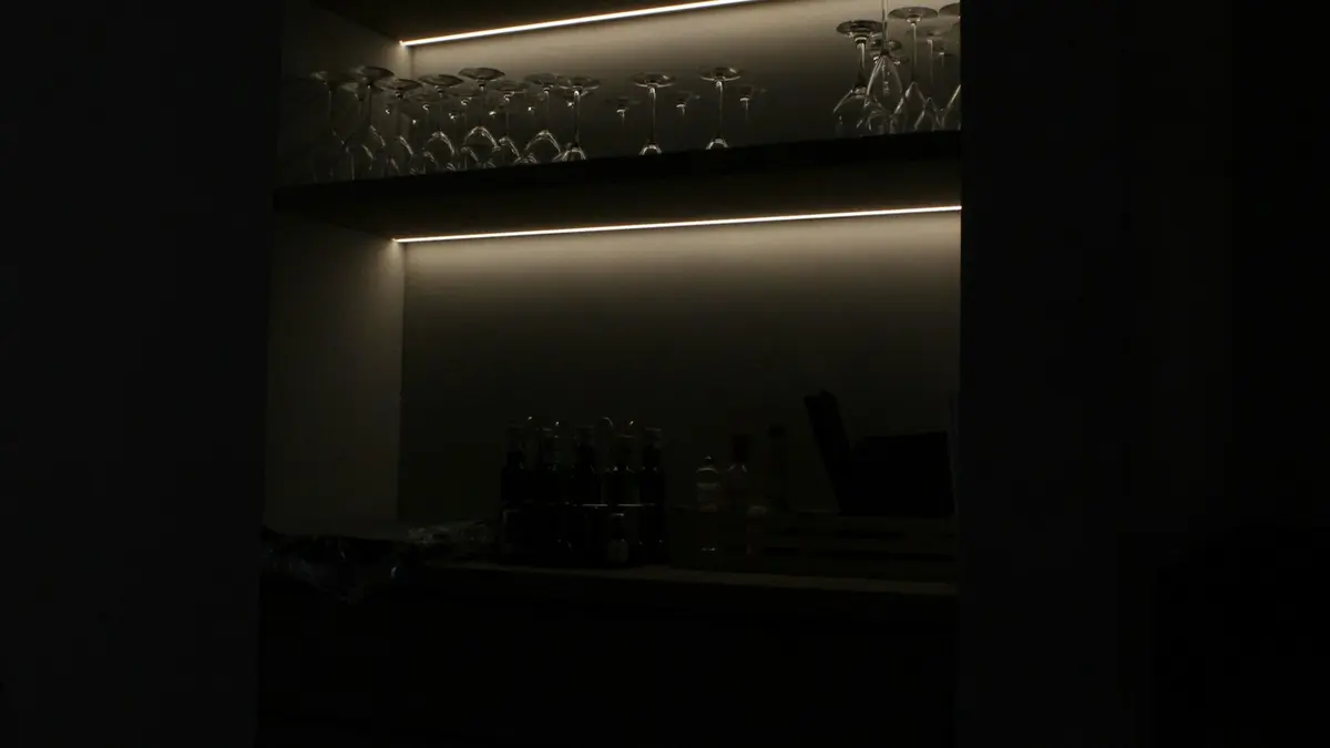 Under-cabinet lighting displaying glassware and bottles on a shelf in low light.