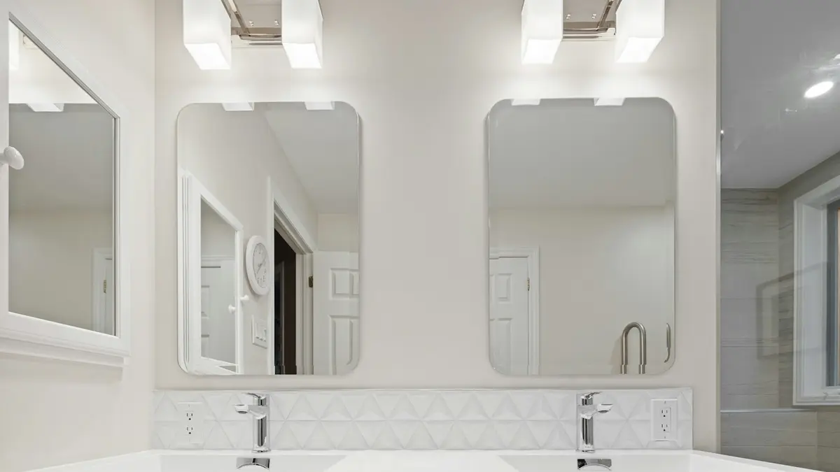 Modern bathroom with dual mirrors and wall-mounted light fixtures above a white vanity.