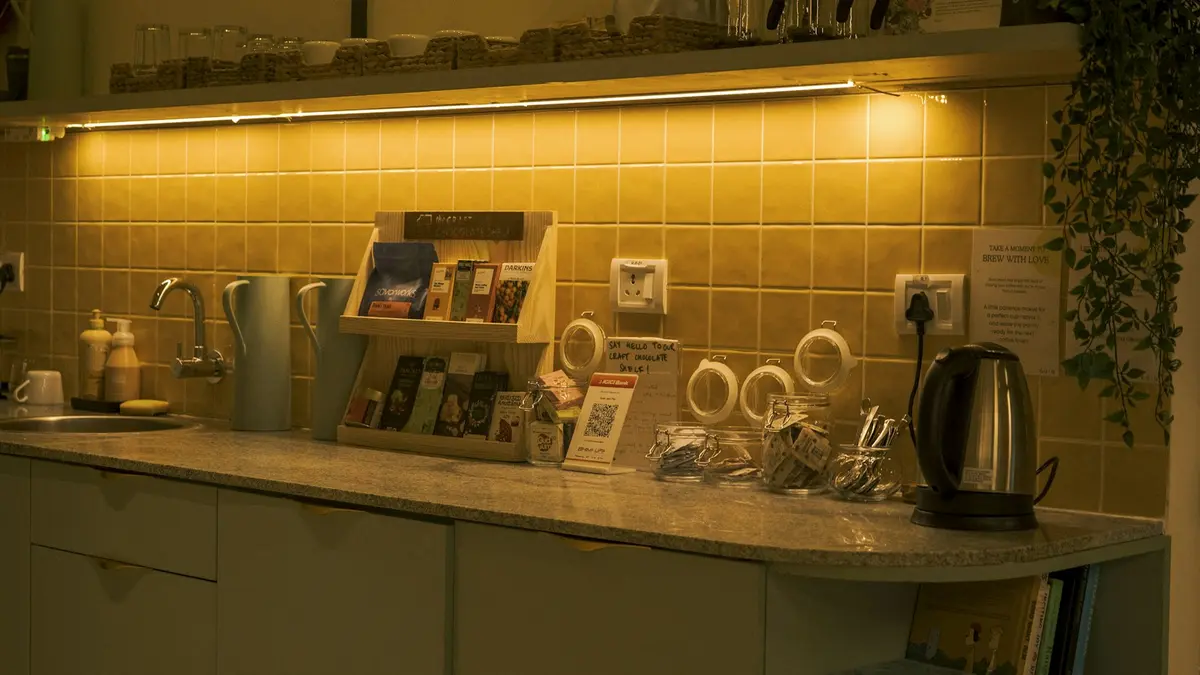 Cozy kitchen counter with warm under-cabinet lighting, featuring utensils, a kettle, and reading materials.